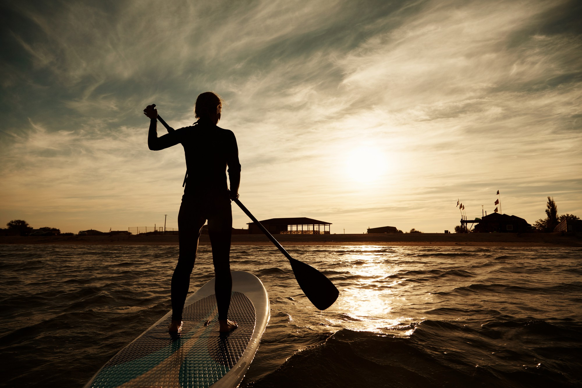 Mujer frente a una puesta de sol haciendo paddle surf